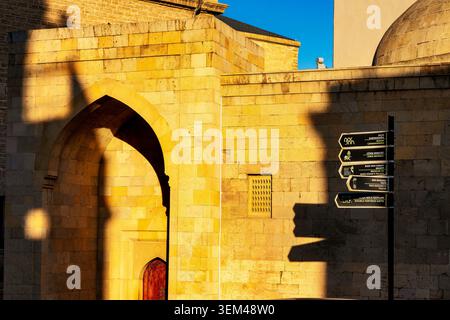 Spitzes Steinportal der Sayyid Yahya Murtuza Moschee mit touristischen Hinweisschildern und dramatischem Schatten in Icheri Sheher. Baku, Aserbaidschan. Stockfoto
