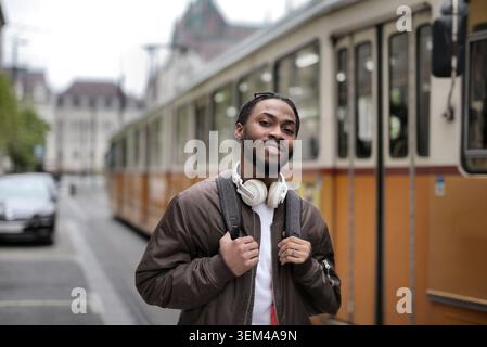 Junger schwarzer Mann mit Kopfhörern, die in einer Straßenbahn lächeln Stockfoto