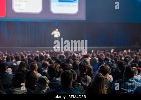 Überfüllter Konferenzsaal mit aufmerksamem Publikum, das den Sprecher auf der Bühne beobachtet, professionelle Veranstaltungsatmosphäre, Präsentationsvisualisierung und fokussierten Teilnehmern. Stockfoto