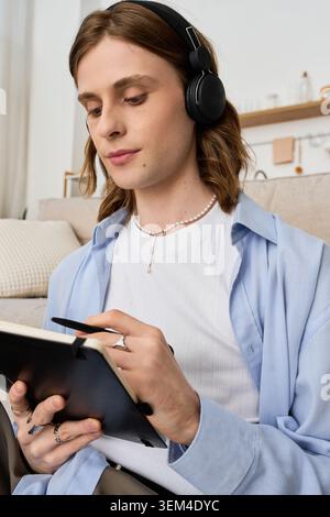 Ein junger Mann, der in Gedanken eingetaucht ist, fängt Ideen ein, während er Kopfhörer in seinem modernen Zuhause trägt. Stockfoto