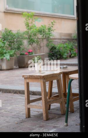 Nahaufnahme eines rustikalen hölzernen Café-Tisches mit einer kleinen Topfpflanze auf einer ruhigen Terrasse mit Kopfsteinpflaster im Innenhof, Paris, Frankreich, Frühjahr 2026. Stockfoto