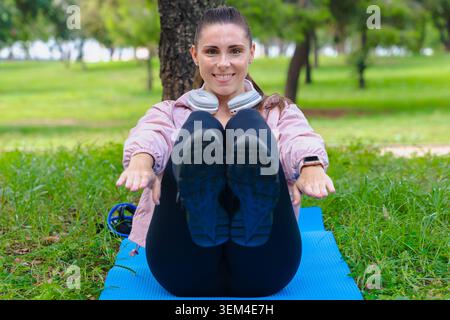 Sportliche Frau, die bauchmuskeln auf Yogamatte im Freien im grünen Park macht, lächelnd Stockfoto