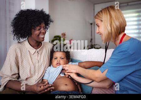 Eine professionelle Krankenschwester, die die Temperatur des Kindes zu Hause misst, bietet medizinische Betreuung und Beratung in einer familiären Umgebung. Stockfoto