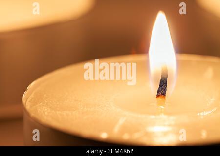 Horizontale Makroaufnahme einer einzelnen brennenden Paraffin-Teelicht-Kerze mit heller Flamme und warmem goldenem Wachs Stockfoto