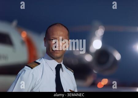 Professioneller Flugkapitän Pilot mit vier goldenen Streifen auf hellblauem Uniformhemd und Krawatte, der bei Sonnenuntergang selbstbewusst auf dem Flughafenaspel steht Stockfoto