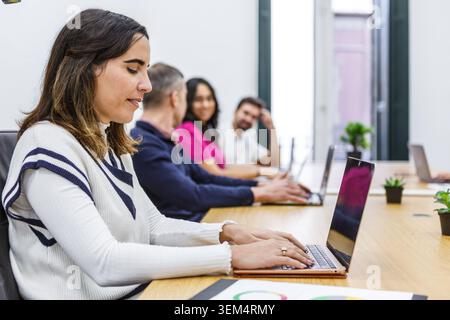 Vier Personen konzentrieren sich in einem hellen Coworking-Raum auf ihre Laptops. Sie kooperieren bei Aufgaben, tauschen Ideen aus und setzen sich mit ihrer Umgebung auseinander. Diese se Stockfoto