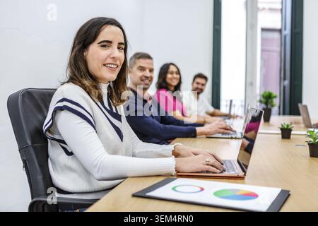 Vier Profis arbeiten an einem langen Schreibtisch in einem Coworking Space. Das Bild zeigt zwei Männer und zwei Frauen, die sich auf ihre Laptops konzentrieren. Stockfoto