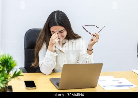 Eine Frau mit langen Haaren trägt ein weißes Hemd und sitzt an einem Schreibtisch in einem Coworking Space. Stockfoto