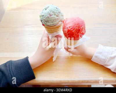 Zwei Kinder halten bunte Eiswaffeln zusammen auf einem Holztisch im Sommer Stockfoto