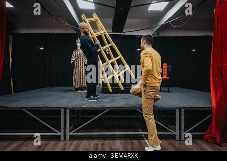 Junge Schauspieler, die auf einer kleinen Theaterbühne mit Leiter und Kostümpuppe Proben Stockfoto