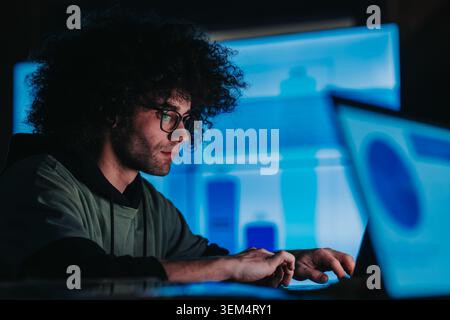 Junge Profis, die spät an einem Notebook arbeiten und Daten mit Teamkollegen auf mehreren Bildschirmen analysieren Stockfoto