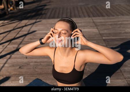 Junge Frau, die mit geschlossenen Augen auf die Lieblings-Playlist hört. Attraktive Frau, die friedliche Entspannung im Freien genießt. Wellness-Selbstpflegekonzept Stockfoto