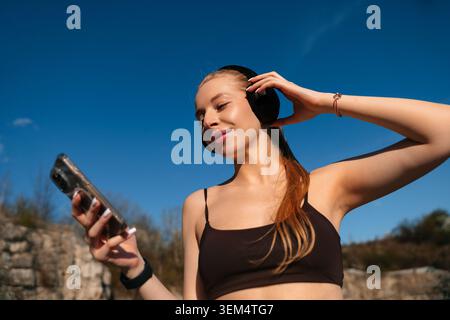 Schöne Frau, die ihre Lieblings-Playlist in kabellosen Kopfhörern genießt. Attraktive Frau mit Smartphone während der Entspannung im Freien. Wellness-Leben Stockfoto
