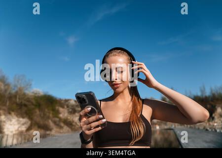 Schönheitsfrau genießt kabellosen Sound neben der natürlichen Landschaft. Attraktive Frau mit Mobiltechnologie während der Entspannungszeit. Aktiver Lifestyle Conce Stockfoto