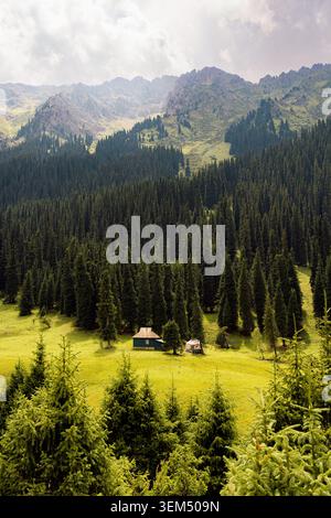 Panoramalandschaft einer abgelegenen Holzhütte und Jurte im Nadelwald des Altyn Arashan-Tals, Kirgisistan Stockfoto
