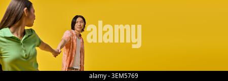 Liebevolles asiatisches Paar, stilvoll gekleidet, Hände haltend und Lächeln in einer hellen Umgebung. Stockfoto
