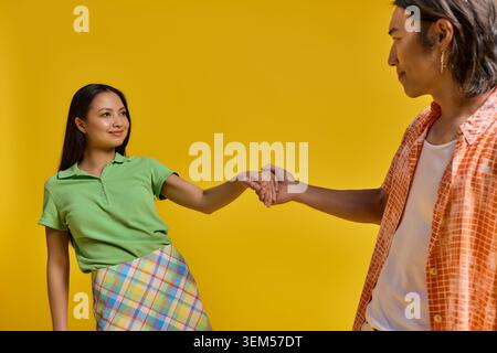 Ein fröhliches asiatisches Paar hält Hände und lächelt in stilvollen Outfits. Stockfoto