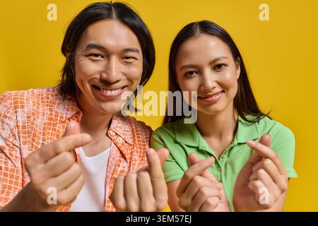 Ein stilvolles junges asiatisches Paar lächelt hell, macht mit den Händen Herzgesten und strahlt Freude aus. Stockfoto