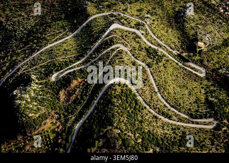 Ein dramatischer Hochwinkelfoto, der direkt nach unten auf die scharfen Haarnadelkurven einer leeren Asphaltstraße blickt, die durch üppig grüne Hänge führt. Stockfoto
