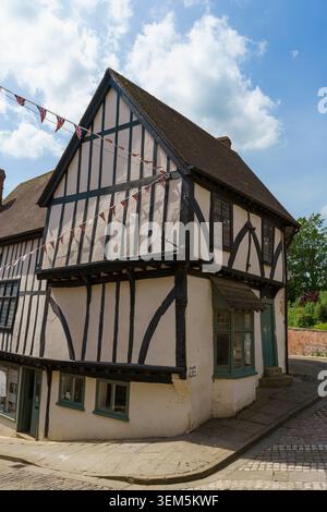 Ein beeindruckendes historisches Fachwerkhaus in Lincoln steht auf dem steilen Hügel, das mit Reihen von Union Jack verziert ist, die vor einem wolkig blauen Himmel stehen. Stockfoto