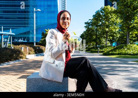 arabische Geschäftsfrau aus dem Nahen Osten im Hijab, die durch die Stadt schlendert - muslimische Frau genießt während ihrer Mittagspause im Freien einen gesunden Salat Stockfoto