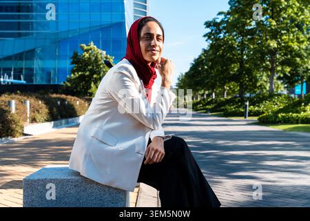 arabische Geschäftsfrau aus dem Nahen Osten im Hijab, die durch die Stadt schlendert - professionelle Frau, die in einem Stadtpark sitzt und selbstbewusst und erfolgreich aussieht Stockfoto