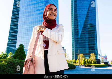arabische Geschäftsfrau aus dem Nahen Osten im Hijab, die durch die Stadt schlendert - muslimische Geschäftsfrau lächelt, fühlt sich selbstbewusst und erfolgreich in einer modernen Stadt Stockfoto