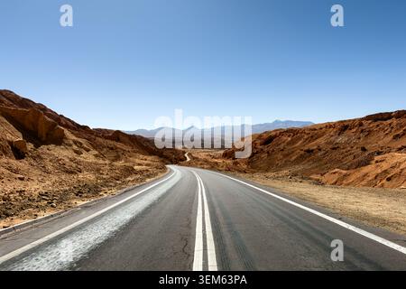 Blick auf eine gewundene Asphaltstraße durch die trockene Wüstenlandschaft des Mars Valley mit rötlichen Felsformationen und entfernten Bergen San Pedro de Atacam Stockfoto