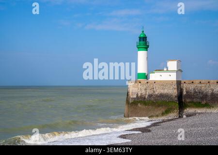 Der weiße Leuchtturm mit grüner Laterne steht auf dem Steinpfeiler von Le Treport, Frankreich. Meereswellen brechen am Kiesstrand im Vordergrund darunter Stockfoto