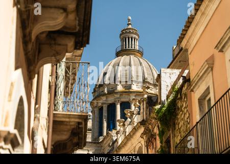 Blick auf die barocke Kuppel des Duomo di San Giorgio aus einer engen Straße mit historischen Gebäuden und Balkonen in Ragusa, Sizilien, Italien. Stockfoto