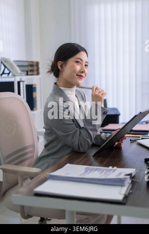 Asiatische junge professionelle Juristin Geschäftsfrau, die Rechtsdokumente mit Stift an modernen Büroarbeitsplätzen überprüft Stockfoto