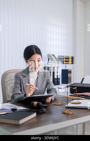 Asiatische Anwältin, die Notizen schreibt, Rechtsdokumente am Bürotisch mit Hamel-Gesetzbüchern überprüft Stockfoto