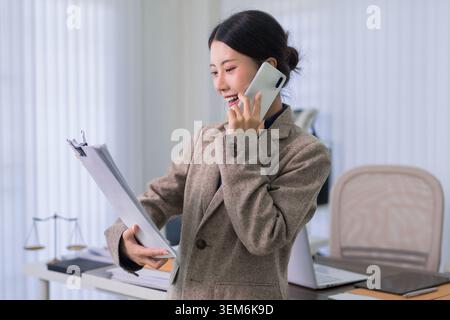 Asiatische Anwältin telefoniert Telefon hält Klemmbrett Überprüfung von Rechtsdokumenten Büro Arbeitsplatz Geschäftskommunikation Stockfoto