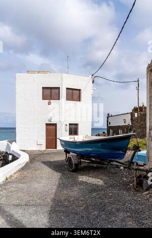 Ein malerisches Boot ruht auf einem Anhänger neben einem weißen Gebäude in Punta Mujeres, Lanzarote. Die Architektur fügt sich in die Küstenlandschaft ein. Stockfoto