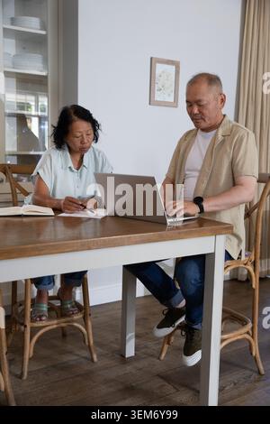 Asiatisches Paar mit einer älteren Frau, die zu Hause am Holztisch sitzt und sich Laptop und Papiere ansieht Stockfoto