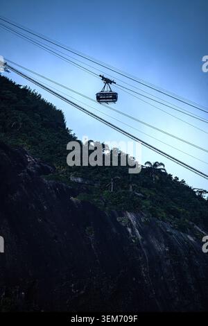 Blick auf die Seilbahn des Sugarloaf Mountain, die über steile felsige Klippen und üppige tropische Vegetation unter einem klaren blauen Himmel in Rio de Janeiro, Bundesstaat Stockfoto