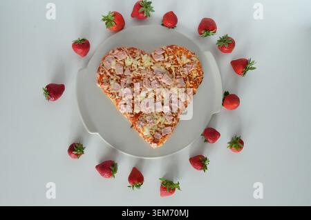 Herzförmige Pizza mit Schinken und Erdbeeren auf einem weißen Teller auf weißem Hintergrund Stockfoto