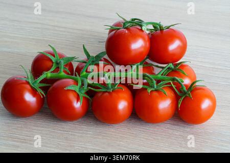Frische Kirschtomaten auf einem Zweig auf hölzernem Hintergrund. Nahaufnahme. Rote Tomaten. Stockfoto
