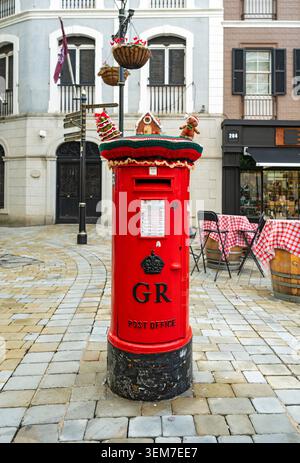 Ein historischer roter britischer Postkasten mit einer Chiffre von König George VI., gekrönt mit festlichem Garn-Graffiti, auf einer gepflasterten Straße, Main Street, Gibraltar Stockfoto