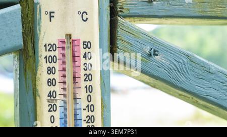Vintage-Thermometer auf einem rustikalen Holzzaun, das Temperaturmesswerte in Fahrenheit und Celsius hervorhebt, die Atmosphäre im Freien und erfasst Stockfoto
