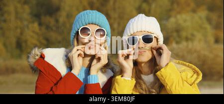 Porträt von glücklichen zwei Freundinnen, die Spaß haben, Schnurrbart in winterlichem Hut, Brille und lustigen Freundinnen im Park zu zeigen Stockfoto