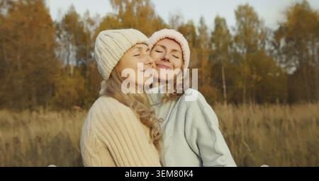 Glückliche Mutter und erwachsene Tochter umarmen, zwei Freundinnen im Herbstpark, fröhliche Freundinnen lächeln zusammen im Freien, tragen Pullover und Hut Stockfoto