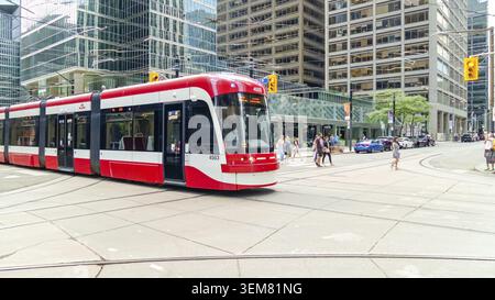 Toronto ON, Kanada - 4. Juli 2022: Die Bombardier-Straßenbahn von TTC fährt durch die belebten Straßen von Toronto, mit Wolkenkratzern und Fußgängern Stockfoto