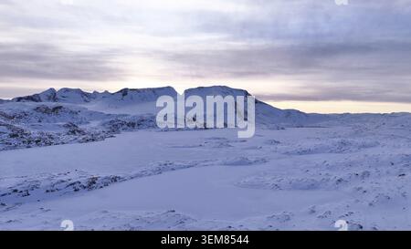 Eine riesige schneebedeckte Berglandschaft in Norwegen mit einem gefrorenen See und einem ruhigen Winterhimmel, die eine ruhige arktische Szene schafft Stockfoto