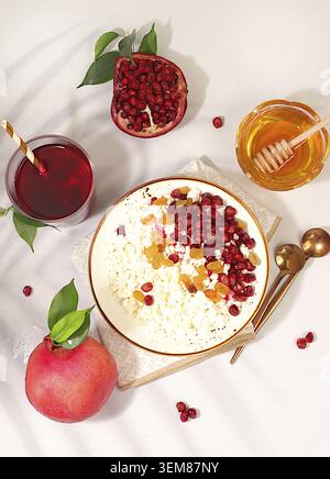 Gesundes Frühstück mit Zutaten. Weicher, körniger Hüttenkäse mit Granatapfelkernen, Rosinen, Honig und Saft auf sonnigem Tisch, natürliches Lebensmittelkonzept, Stockfoto