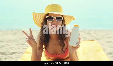 Sommerurlaub, glückliche lächelnde Frau in Touristenhut mit Sonnencreme, am Strand vor Meeresgrund auf dem Sand liegend Stockfoto