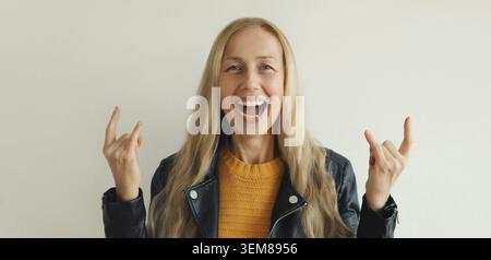 Porträt einer glücklichen, stilvollen, emotionalen, reifen Frau, die mit verrücktem Ausdruck überglücklich ist und Rock-Symbol mit erhobenen Händen macht, modische weibliche Havin mittleren Alters Stockfoto