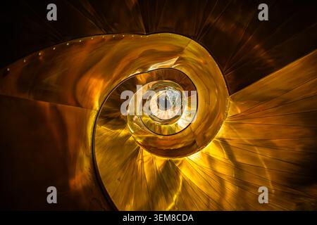Abstraktes Architekturfoto einer goldenen Wendeltreppe von oben, mit eleganten Kurven, geometrischer Symmetrie und reflektierenden metalli Stockfoto