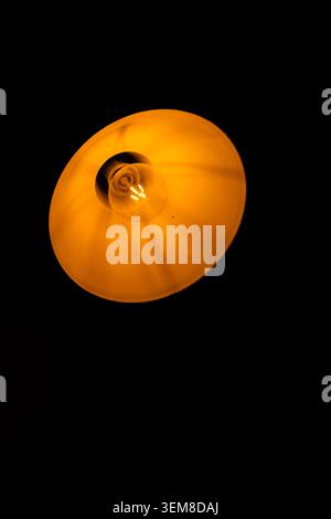 Nahaufnahme einer glühenden Glühlampe in einem Vintage-Lampenschirm aus Industriemetall. Warme goldene Beleuchtung schafft eine abstrakte minimalistische Co Stockfoto