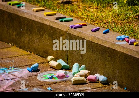 Verschiedene bunte Kreideflächen auf dem Bürgersteig in hellem Sonnenlicht auf einem Bürgersteig in der Nähe einer Bordsteinkante verstreut. Zeigt die Outdoor-Kreativität von Kindern, künstlerische Ausdrucksformen Stockfoto